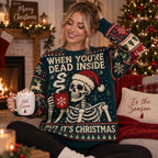 woman smiling in a dark green ugly christmas sweater by a fireplace