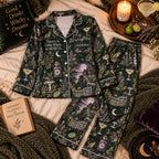flat lay of dark green witchy botanical satin pajama set with haunted house print