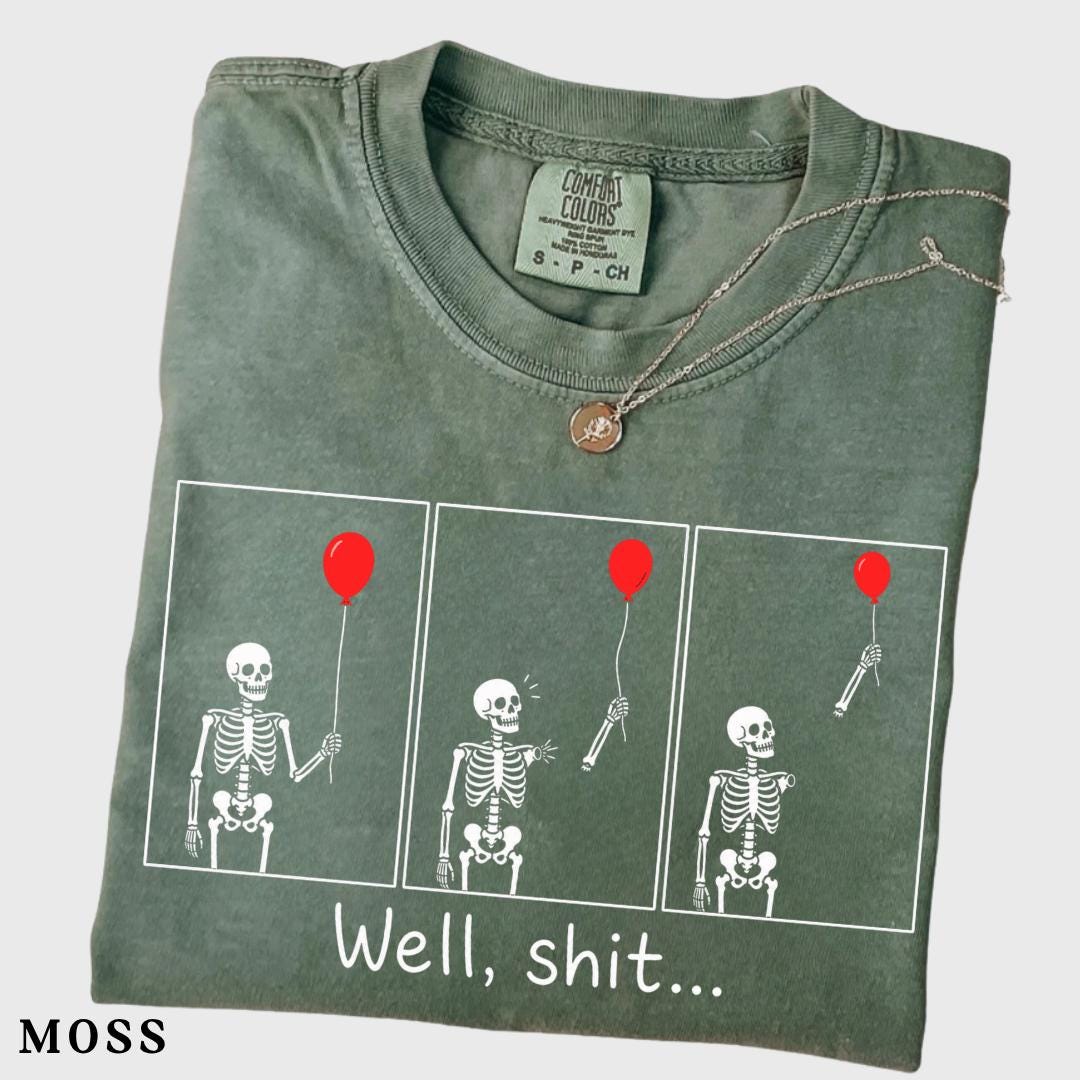 folded moss green graphic tee with skeleton and red balloon comic print